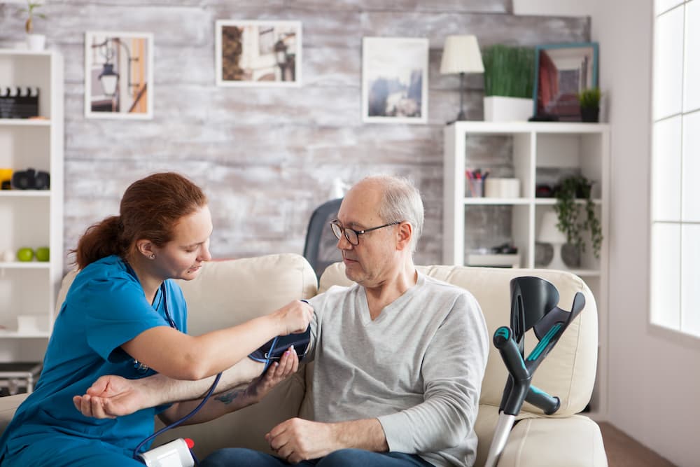 A home health nurse checking an older man's blood pressure in his living room