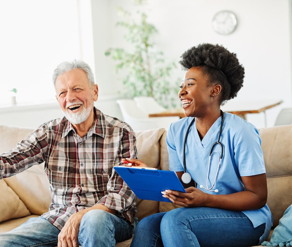 A home health nurse laughing with an older man during a visit at home